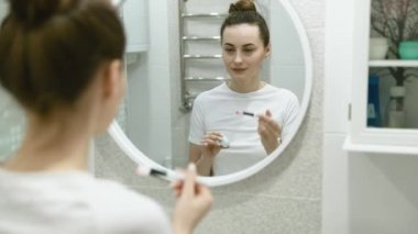 Güzel bir kadının portresi makyaj yapıyor. Evde hazırlanıyor. Aynaya bakıyor ve doğal cildinin tadını çıkarıyor.