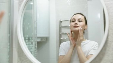 Güzel bir kadının portresi makyaj yapıyor. Evde hazırlanıyor. Aynaya bakıyor ve doğal cildinin tadını çıkarıyor.