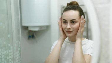 Güzel bir kadının portresi makyaj yapıyor. Evde hazırlanıyor. Aynaya bakıyor ve doğal cildinin tadını çıkarıyor.