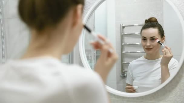 年轻漂亮的女人把面霜涂在她的颧骨上 看着镜子 用圆形动作 皮肤护理 天然化妆品和面部护理的方式涂上面霜 — 图库视频影像