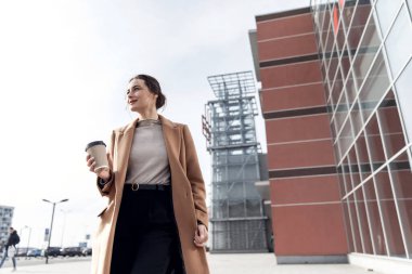 Akıllı telefonlu genç bir Cousian kadın caddenin karşısında duruyor. Bina geçmişi bulanık. Siyah süitte, bir fincan kahve ve telefonla güzel bir kızın moda fotoğrafı.