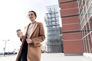 Kafası ve omuzları ağır çekimde. Güzel ve kendine güvenen genç bir kadının resmi. Açık havada kameraya bakıp gülümsüyor.