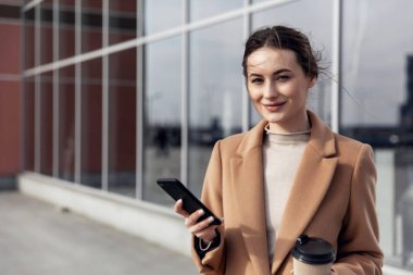 Kafası ve omuzları ağır çekimde. Güzel ve kendine güvenen genç bir kadının resmi. Açık havada kameraya bakıp gülümsüyor.