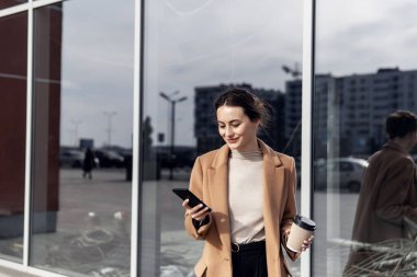 İş kadını akıllı telefonunu kullanarak büyüleyici bir şekilde gülümsüyor. Kadın güneşli günün ve komik sohbetin tadını çıkarıyor. Telefonuna faiziyle yazı yazıyormuş. Esmer kız. Başarılı bir kadın. Telefonlar. Uygulamalar.