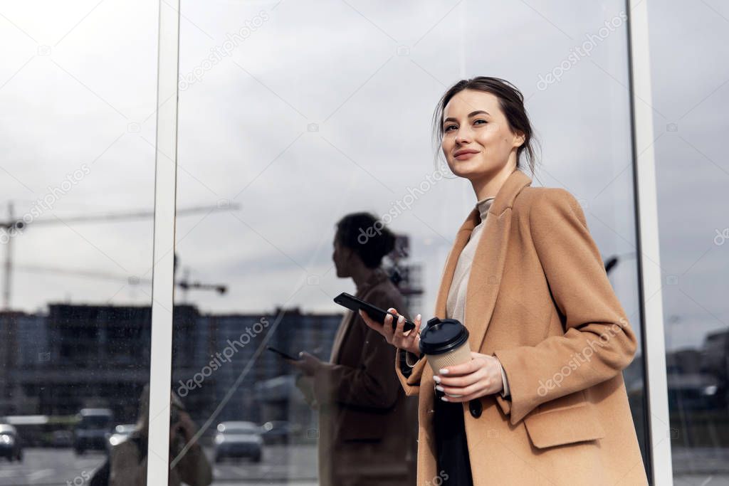 Business Woman smiling charmingly, using her Smartphone. Female enjoying sunny day and funny conversation. Typing on her Phone with Interest. Brunette Girl. Successful Woman. Phones. Apps.