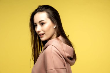 Mavi kulaklıklı enerji kızı stüdyoda sarı arka planda müzik dinliyor. Beyaz tişört ve şort giyiyor. Kuyruktaki uzun kıvırcık saçlar atlarken tepemizde uçuşuyor..