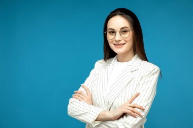 Mavi arka planda kollarını kavuşturmuş gülümseyen kuzen kadının portresi.