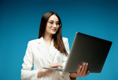 Mavi arka planda izole edilmiş dizüstü bilgisayar kullanan zeki güzel bir genç kız.