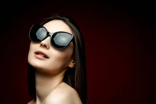Model busana berkacamata hitam, wanita muda yang cantik. lstudio shot, latar belakang merah — Stok Foto