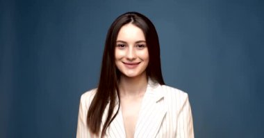 Mavi duvara karşı gülümseyen genç bir iş kadını. Beyaz gömlekli. Kameraya bak.