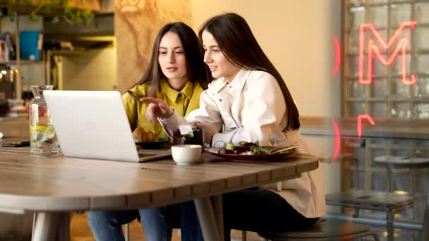两个漂亮的黑发女人坐在现代咖啡馆里 开着笔记本电脑 笑着和说话 穿着鲜艳衣服的少女们享受着无线设备带来的闲暇时光 — 图库视频影像