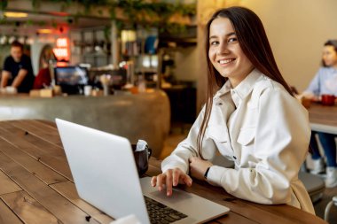 Sabah kahvaltısı sırasında rahat bir kafede laptopta çalışan modaya uygun giyinmiş çekici bir kadın serbest yazar. Kahverengi saçlı, gülümseyen ve kamerada poz veren güzel kızlar..