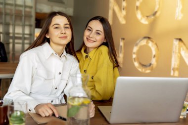 Şık giyinmiş neşeli genç bayanlar seyahat için yeni bir yer seçtikten sonra birbirlerine sarılıyorlar. Kahverengi saçlı güzel bayanlar online bilet almak için dizüstü bilgisayar kullanıyorlar..