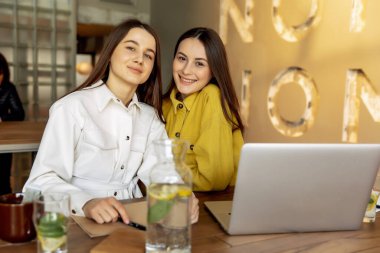 Şık giyinmiş neşeli genç bayanlar seyahat için yeni bir yer seçtikten sonra birbirlerine sarılıyorlar. Kahverengi saçlı güzel bayanlar online bilet almak için dizüstü bilgisayar kullanıyorlar..