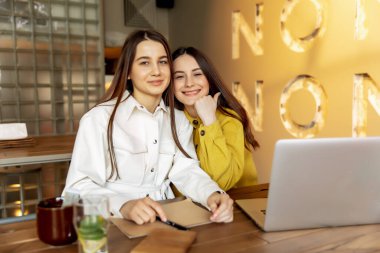 Şık giyinmiş neşeli genç bayanlar seyahat için yeni bir yer seçtikten sonra birbirlerine sarılıyorlar. Kahverengi saçlı güzel bayanlar online bilet almak için dizüstü bilgisayar kullanıyorlar..