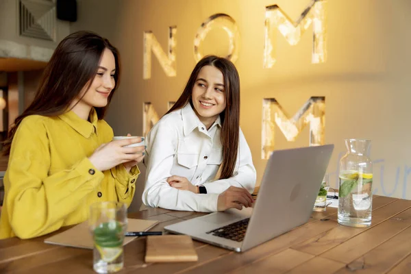 两个穿着鲜艳衣服的女性朋友坐在舒适的咖啡店里 坐在笔记本电脑上在线订机票 快乐的棕色头发的女人计划新的暑假之旅 — 图库照片