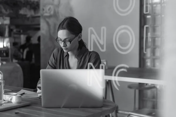 Şık gözlüklü, odaklanmış iş kadını laptopta çalışan, kafeye odaklanmış, kafeteryada bilgisayar ve kapuçinoyla çalışan, serbest çalışan, online okuyan, internette gezinen, faturaları kontrol eden,
