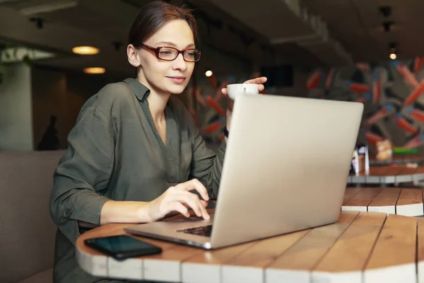 Şık gözlüklü, odaklanmış iş kadını laptopta çalışan, kafeye odaklanmış, kafeteryada bilgisayar ve kapuçinoyla çalışan, serbest çalışan, online okuyan, internette gezinen, faturaları kontrol eden,