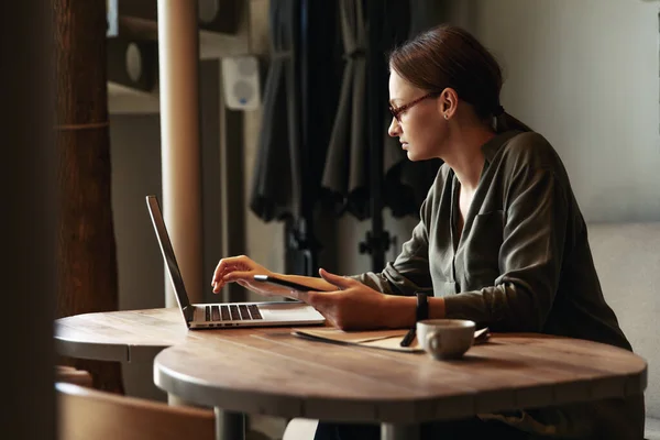 Şık gözlüklü, odaklanmış iş kadını laptopta çalışan, kafeye odaklanmış, kafeteryada bilgisayar ve kapuçinoyla çalışan, serbest çalışan, online okuyan, internette gezinen, faturaları kontrol eden,