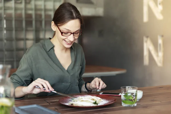戴着时髦眼镜的女商人坐在咖啡店里的笔记本电脑旁 一边吃早餐 一边端着一杯咖啡 — 图库照片