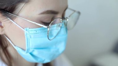 Gözlüklü, sağlık hizmetleri uzmanı bir kadının hastanede ameliyat maskesi takarken ön görüntüsü. Coronavirus 'taki sağlık çalışanları Covid19 salgını