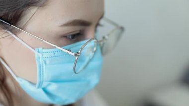 Gözlüklü, sağlık hizmetleri uzmanı bir kadının hastanede ameliyat maskesi takarken ön görüntüsü. Coronavirus 'taki sağlık çalışanları Covid19 salgını