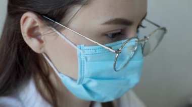 Gözlüklü, sağlık hizmetleri uzmanı bir kadının hastanede ameliyat maskesi takarken ön görüntüsü. Coronavirus 'taki sağlık çalışanları Covid19 salgını