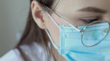 Gözlüklü, sağlık hizmetleri uzmanı bir kadının hastanede ameliyat maskesi takarken ön görüntüsü. Coronavirus 'taki sağlık çalışanları Covid19 salgını