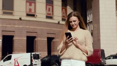 Caddede yürüyen ve cep telefonu kullanan büyüleyici gülüşlü güzel kadın. Modern güneş gözlüğü takmak ve şık kıyafetler giymek. Sıradan giyimli, çekici bir kadın.
