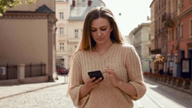 Caddede yürüyen ve cep telefonu kullanan büyüleyici gülüşlü güzel kadın. Modern güneş gözlüğü takmak ve şık kıyafetler giymek. Sıradan giyimli, çekici bir kadın.