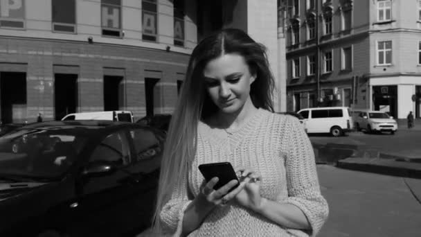 美丽的女人，带着迷人的微笑在街上散步，用手机。戴着现代太阳镜，穿着时髦的衣服。衣冠楚楚的年轻迷人女人 — 图库视频影像