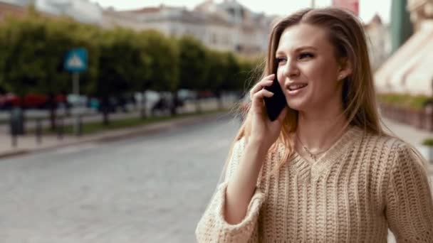 Счастливая молодая женщина разговаривает по телефону во время прогулки по улице. close up — стоковое видео