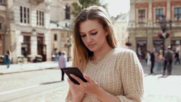 Close-up van aantrekkelijke jonge zakenvrouw lopen op stedelijke straat en met behulp van moderne smartphone buiten, zon, slow motion — Stockvideo