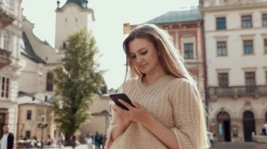 Caddede yürüyen ve cep telefonu kullanan büyüleyici gülüşlü güzel kadın. Modern güneş gözlüğü takmak ve şık kıyafetler giymek. Sıradan giyimli, çekici bir kadın.