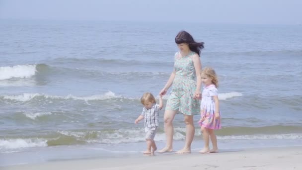 Happy family on the beach. Mother holds the arms of her son and daughter walking along the seashore. Slow motion.