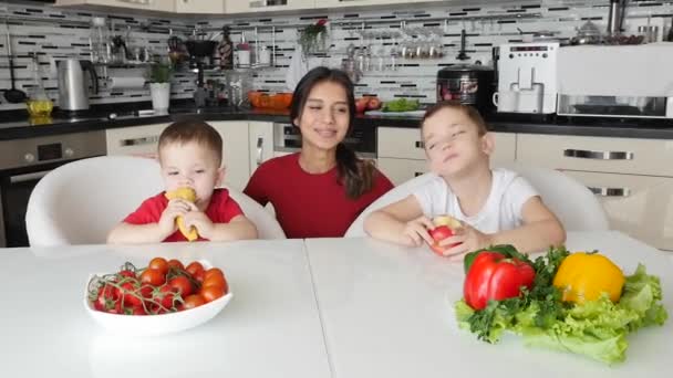 Діти з нянею їдять фрукти і посміхаються за столом . — стокове відео