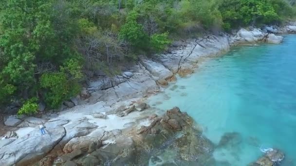 AERIAL. Mujer joven de pie sobre las rocas de la costa oceánica en los trópicos . — Vídeo de stock