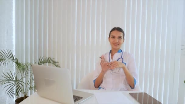 Γιατρός, πληκτρολογώντας κείμενο σε ένα φορητό υπολογιστή. Νεαρά ασιατικές ελκυστική γυναίκα γιατρός κάθεται στο γραφείο στο τραπέζι. Ασπίδα με το λογότυπό σας σε ένα φορητό υπολογιστή — Αρχείο Βίντεο