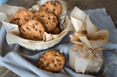 Parşömen kağıdında çikolata ve altın kurdeleli yulaflı kurabiyeler. Masada keten bir peçete var..