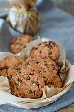 Parşömen kağıdında çikolata ve altın kurdeleli yulaflı kurabiyeler. Masada keten bir peçete var..