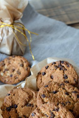 Parşömen kağıdında çikolata ve altın kurdeleli yulaflı kurabiyeler. Masada keten bir peçete var..