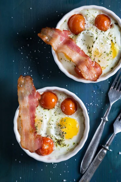 Baked eggs with cherry tomatoes, bacon and greens