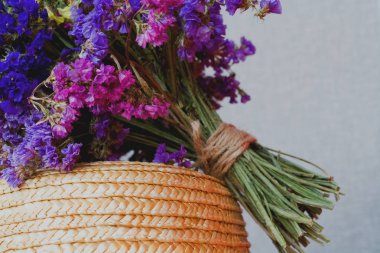 Hasırdan örülmüş şapkanın arka planında bir ton kuru çiçek buketi. Violet.