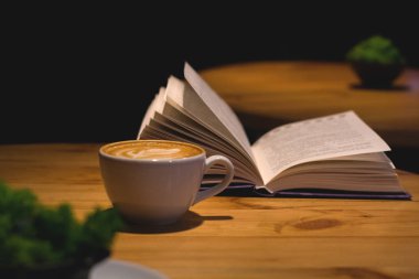 Kahve dükkanında seramik bardak kapuçino, açık bir kitapla ahşap bir masada desenli. Latte sanatı. Sabah içkisi. Kafein.