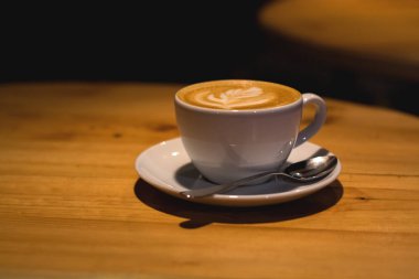 Kahve dükkanında seramik kupa ve ahşap boş masa üzerinde kapuçino. Latte sanatı. Sabah içkisi. Kafein.