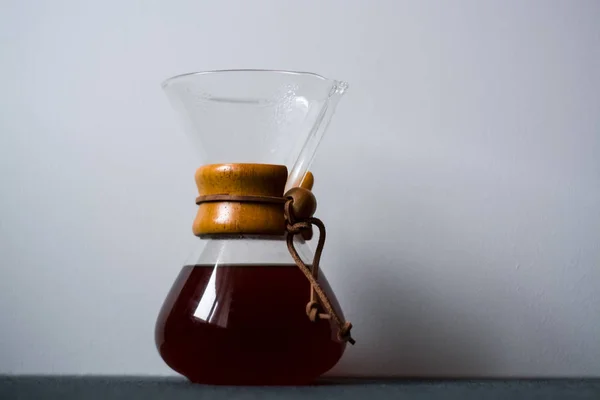 Glass container filled with black coffee on one-ton white background with reflection of large and unusual shadows.