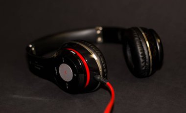Siyah arka planda, kırmızı elementler ve kordon ile müzik dinlemek için büyük kulaklıklar. 