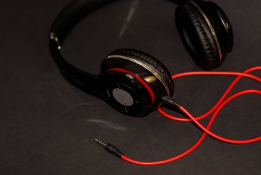 Siyah arka planda, kırmızı elementler ve kordon ile müzik dinlemek için büyük kulaklıklar. 