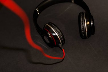 Siyah arka planda, kırmızı elementler ve kordon ile müzik dinlemek için büyük kulaklıklar. 