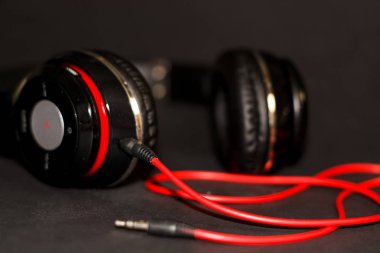 Siyah arka planda, kırmızı elementler ve kordon ile müzik dinlemek için büyük kulaklıklar. 